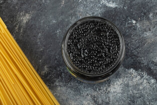 A glass plate of black sturgeon caviar with uncooked pasta . 