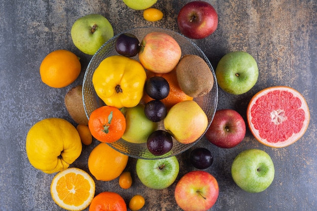 Стеклянная тарелка свежих фруктов поверх многих фруктов.