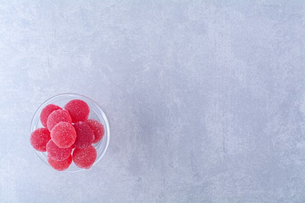 회색 표면에 붉은 설탕 과일 젤리 사탕으로 가득 찬 유리 접시