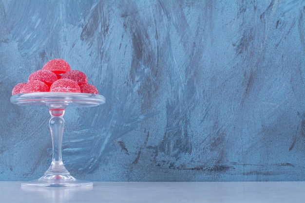 A glass plate full of red sugary fruit jelly candies on gray table. 