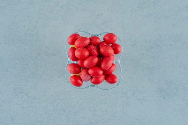 A glass plate full of sweet delicious red candies on a white surface
