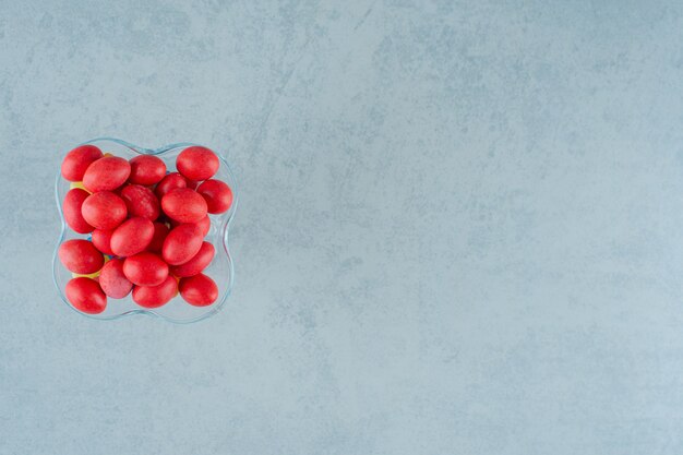 A glass plate full of sweet delicious red candies on a white surface