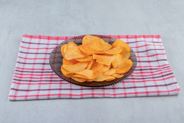 Glass plate of spicy chips placed on stone.
