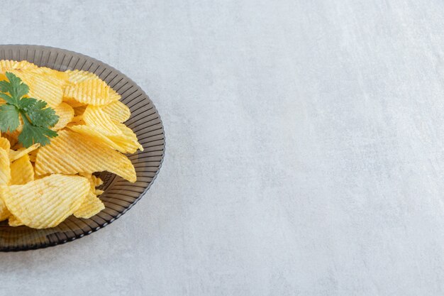 Glass plate of tasty ripple chips on stone.