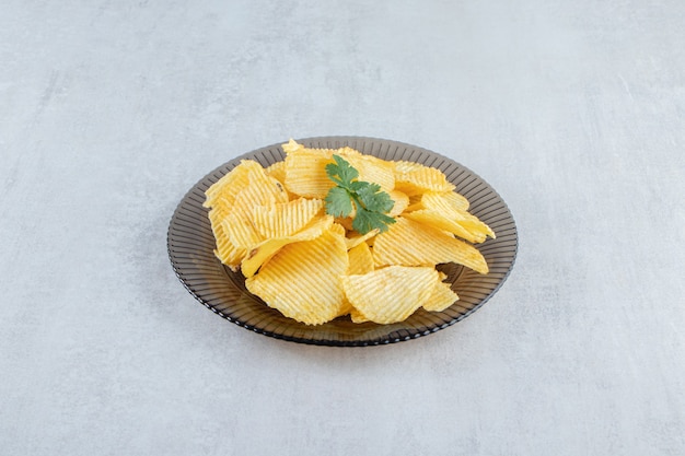 Glass plate of tasty ripple chips on stone.