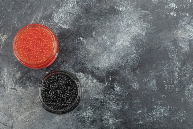 Glass plates full of red and black caviar on a marble table. 