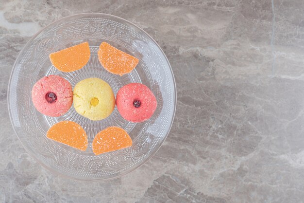 Piatto di vetro con biscotti e caramelle gommose su superficie di marmo