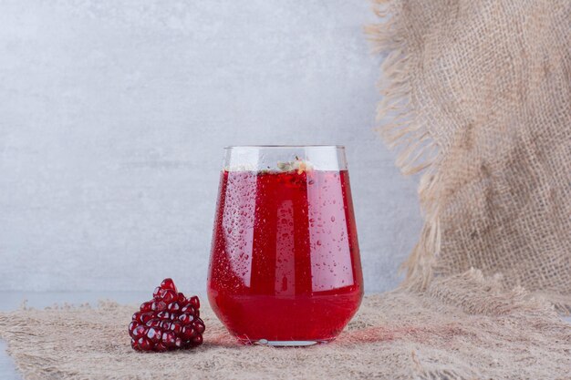 A glass of pomegranate juice on burlap with seeds.