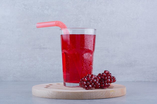 A glass of pomegranate juice on wooden piece with straw.