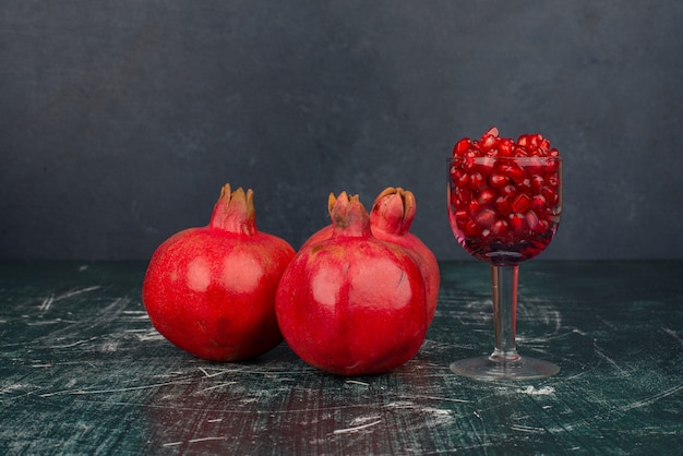 Glass of pomegranate seeds and pomegranate on marble surface.