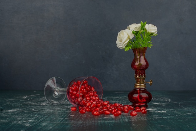 Bicchiere di semi di melograno e fiori bianchi in vaso.