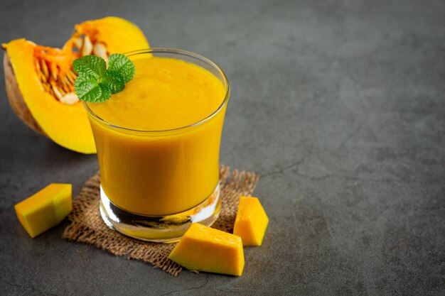 a glass of pumpkin juice and chopped raw pumpkins place on dark floor