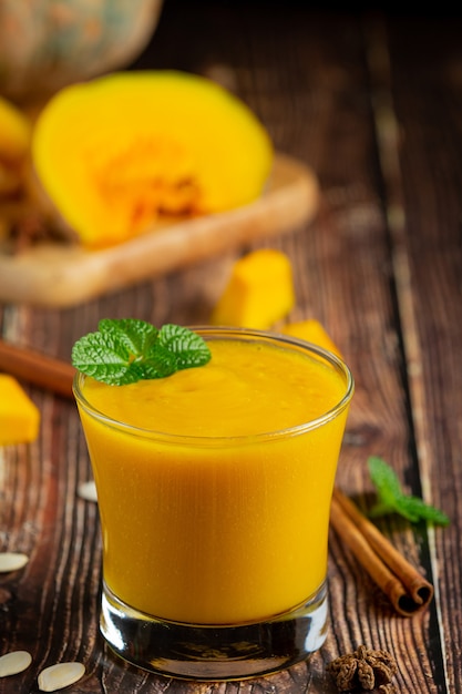 Free photo a glass of pumpkin juice and chopped raw pumpkins place on wooden  floor