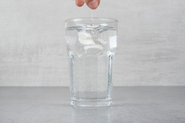 Foto gratuita un bicchiere di acqua fredda pura su una superficie grigia