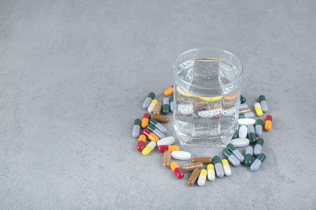 Free photo a glass of pure water with colorful pills on gray surface