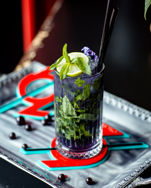 A glass of purple mojito with purple flower lime and mint