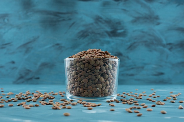 Glass of raw dry buckwheat placed on blue surface.