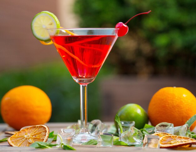 A glass of red alcohol cocktail with lime slice and cherry