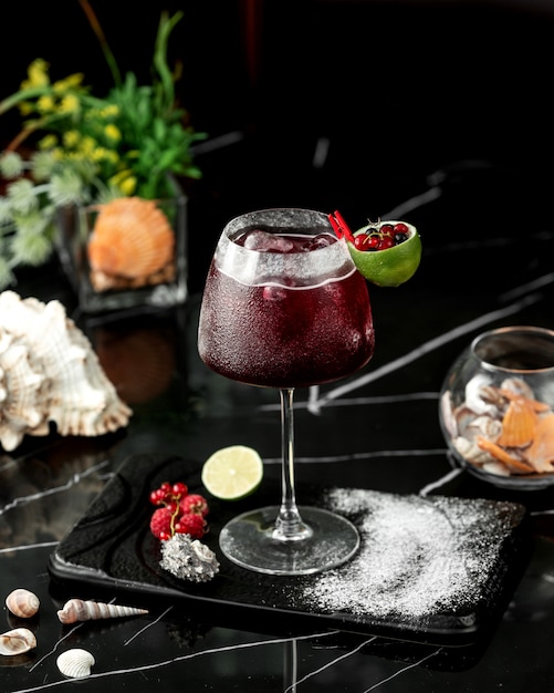 A glass of red cocktail garnished with lime zest and cranberries