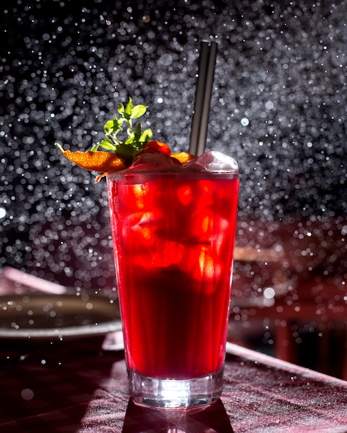A glass of red cocktail garnished with orange slices in dark background with light