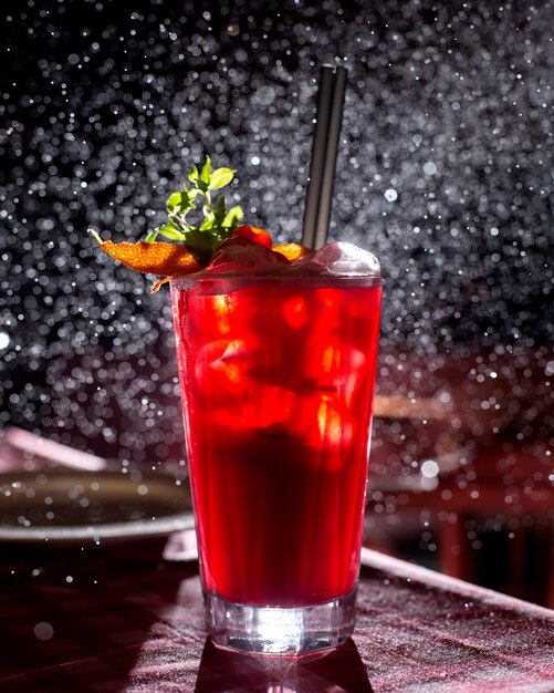 A glass of red cocktail garnished with orange slices in dark background with light