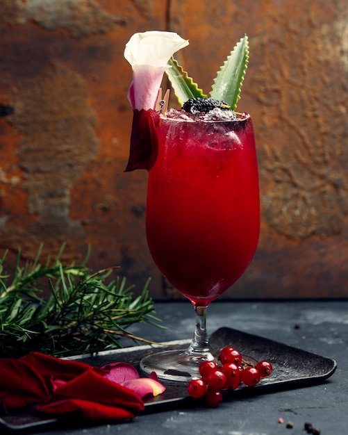 A glass of red drink with ice and aloe leaves