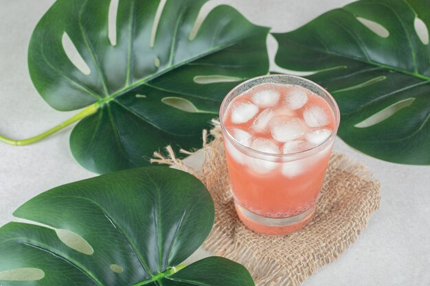 A glass of red juice with ice cubes on burlap