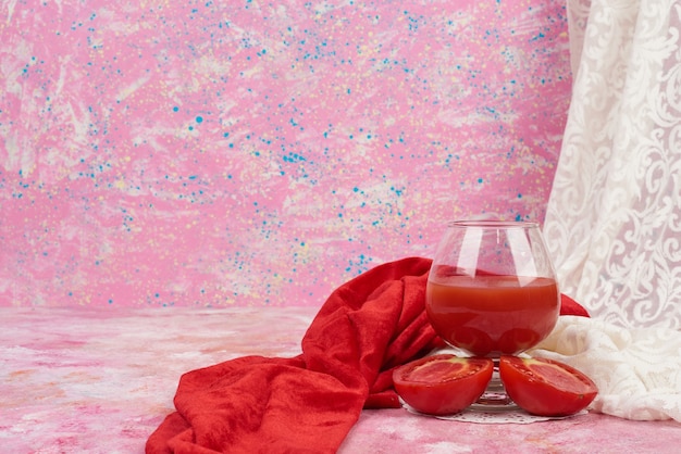 A glass of red juice with tomatoes around.