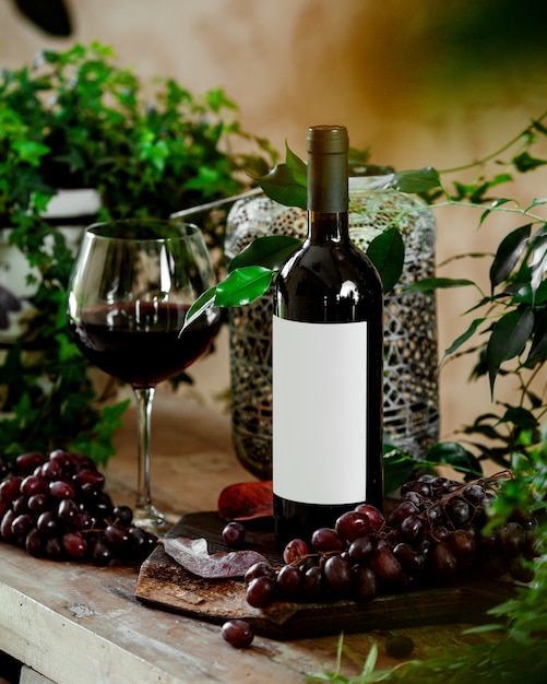 Foto gratuita un bicchiere di vino rosso e una bottiglia di vino rosso sul tavolo con uva rossa