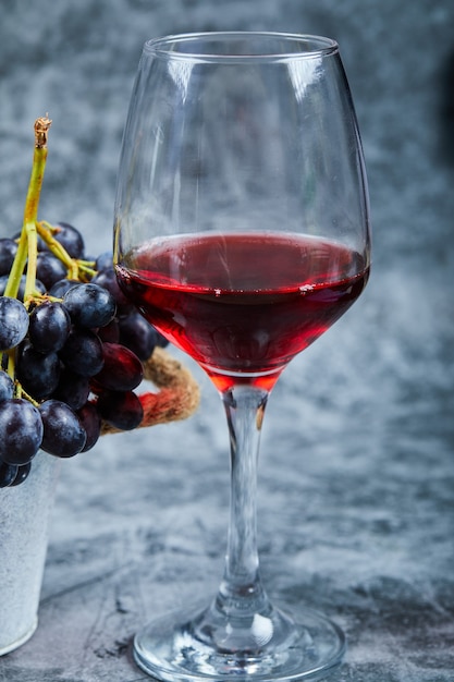 Бокал красного вина на мраморном фоне с виноградом. Фото высокого качества