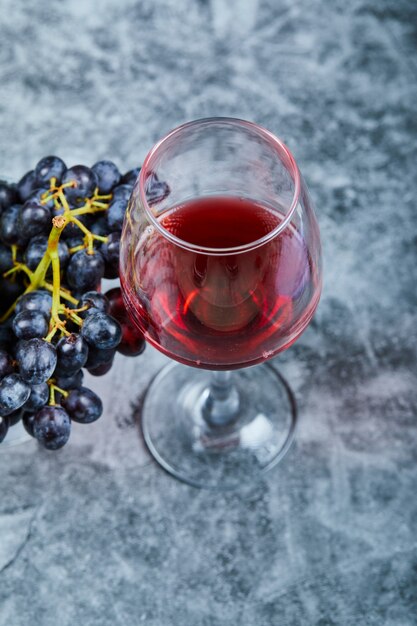 A glass of red wine on marble with grapes.