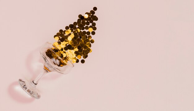 Glass spilling golden confetti on pink background