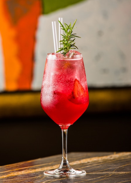 A glass of strawberry cold cocktail with fresh rosemary leaves and pipes