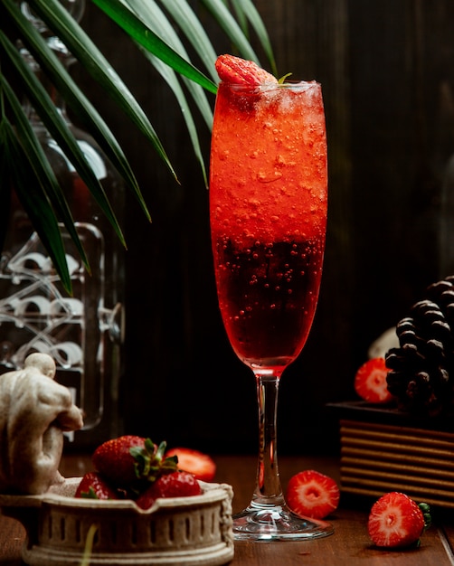 A glass of strawberry fizzy beverage garnished with strawberries