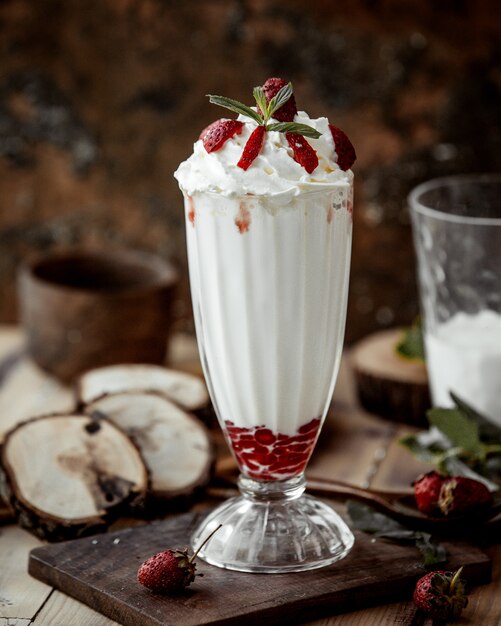 A glass of strawberry milkshake with strawberry pieces and whipped cream