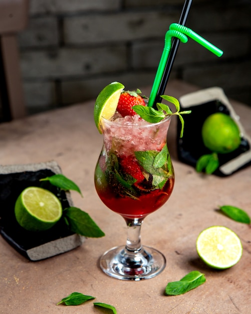 A glass of strawberry mojito with mint lime and strawberries