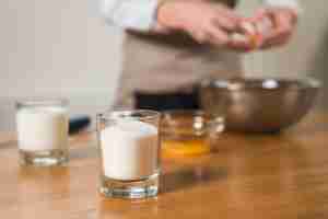 Free photo glass of sugar at foreground with blur woman breaking egg in the bowl