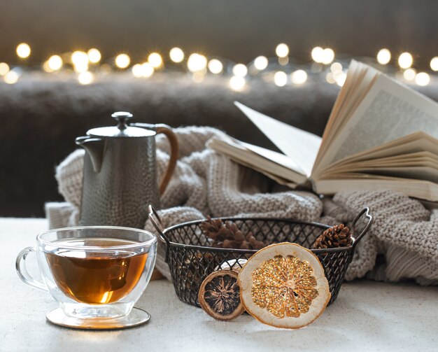 Glass tea cup, teapot and book with knitted element. The concept of home comfort and warmth.