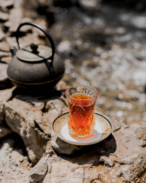 A glass of tea on the ground with black iron kettle.