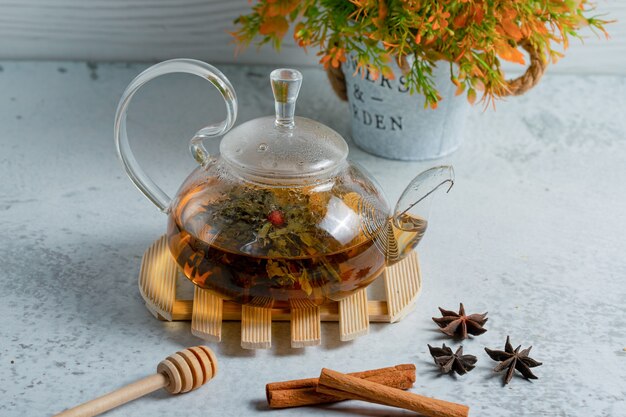 Glass tea pot full with freshly brewed tea on grey wall.