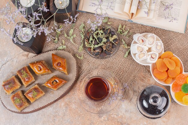 Glass of tea, sweets and traditional various baklavas on marble table.