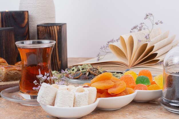 Glass of tea, various sweets and dried apricots on marble table.