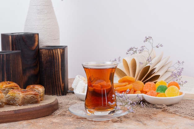 Glass of tea, various sweets and dried apricots on marble table.