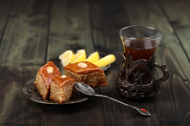 A glass of tea with caucasian pakhlava and lemon on a rustic table.