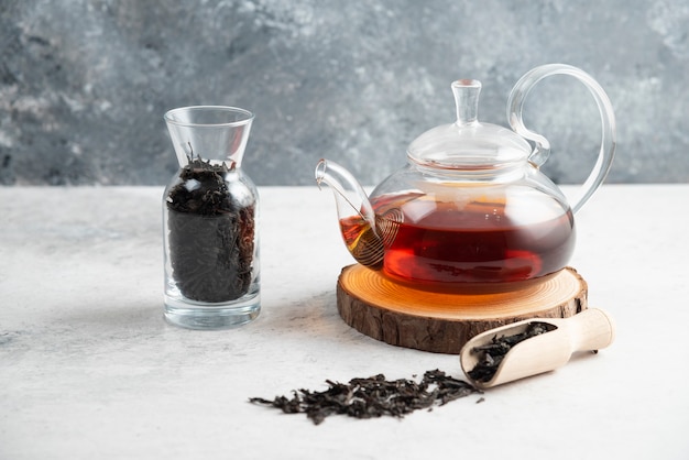 A glass teapot with dried loose teas and a wooden spoon.