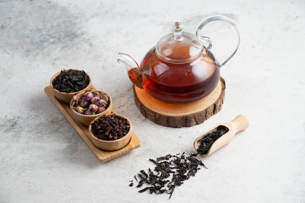 A glass teapot with wooden bowls of loose teas.