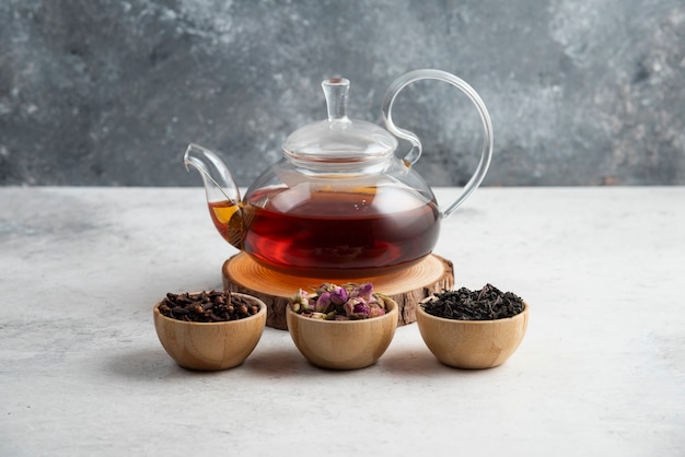 A glass teapot with wooden bowls of loose teas.