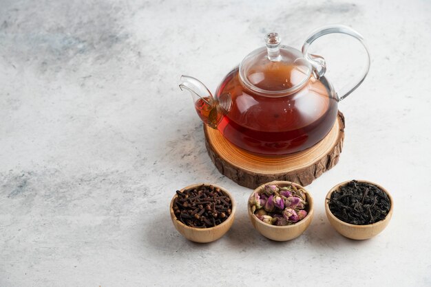 A glass teapot with wooden bowls of loose teas.