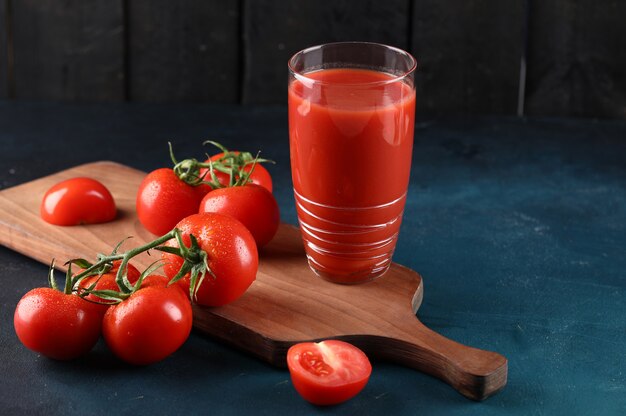 A glass of tomato juice and some fresh tomatoes on the wooden board.