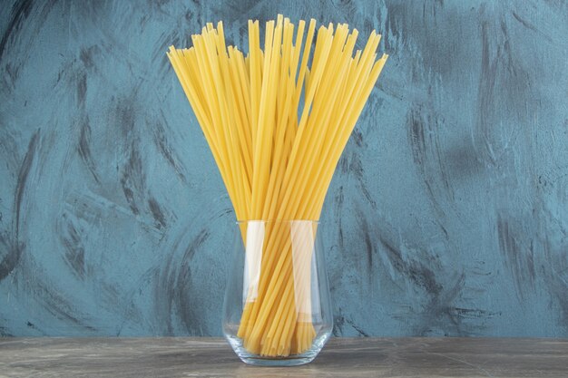 Glass of uncooked tube spaghetti on marble surface.